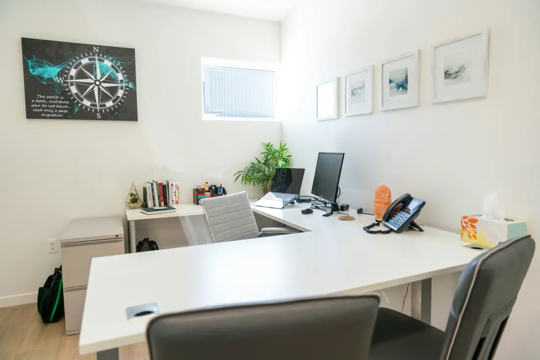 A bright office with desks, a computer and a plant