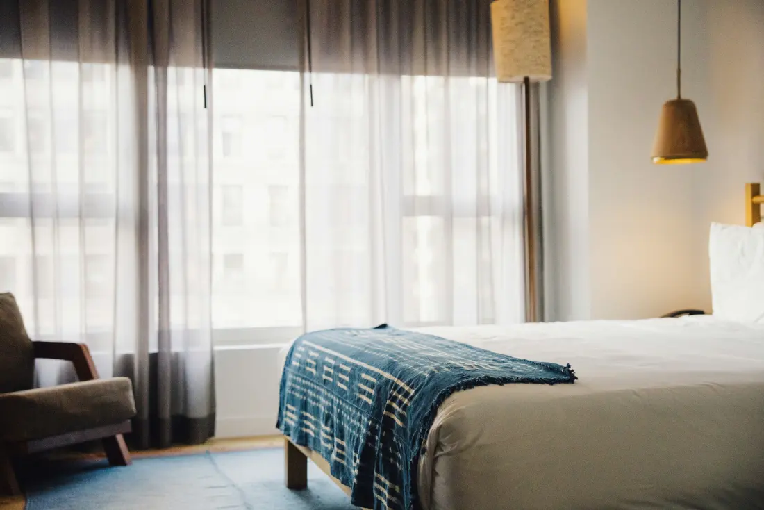 A hotel room with a made bed and a tall window